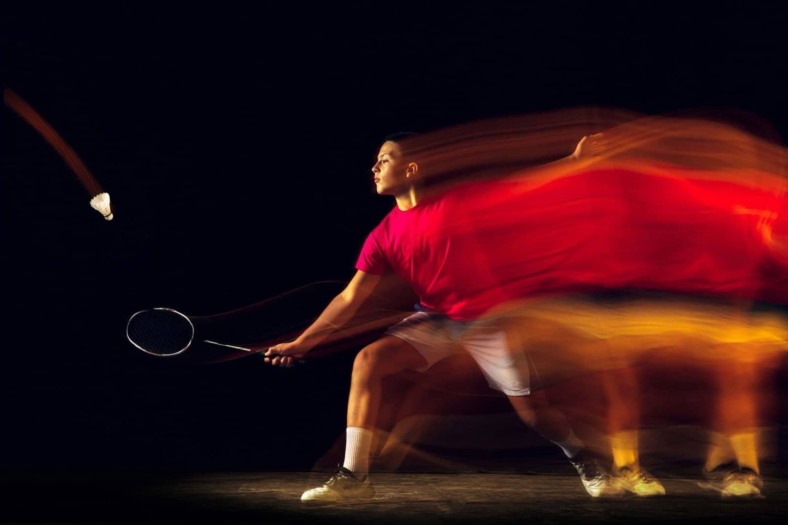 Joueur de badminton Csme 95 arborant une raquette et un volant, t-shirt rouge et short blanc